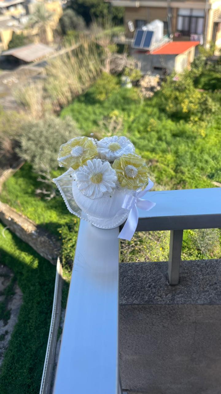 Decorative soap flower arrangement with white and yellow flowers on a railing with a garden view.