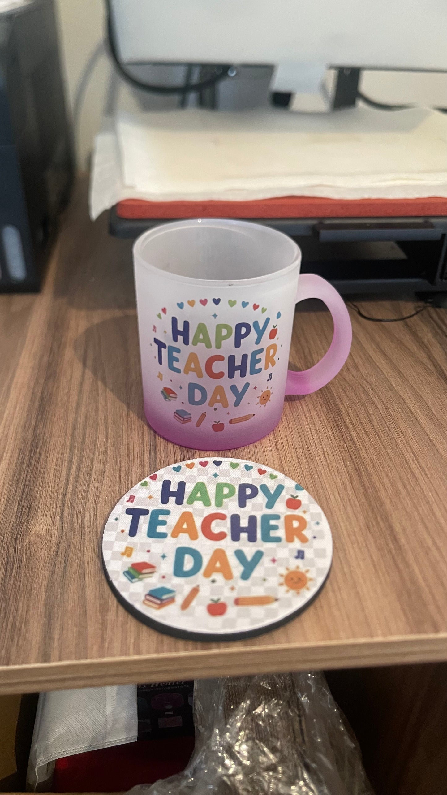 Red Mug and coaster with 'Happy Teacher Day' text on a wooden surface.