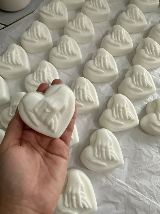 White heart-shaped soap favors with raised hand design arranged on tissue paper