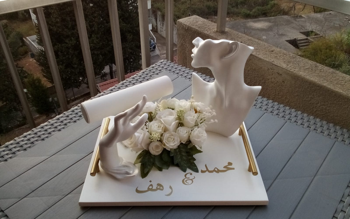 Personalized wedding keepsake tray with white couple sculpture, flowers, gold accents, and Arabic names